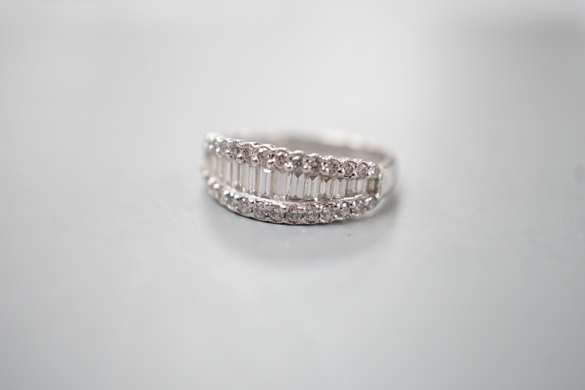 A modern white metal, graduated baguette cut diamond set half hoop ring, with diamond chip borders, size O, gross weight 5 grams.